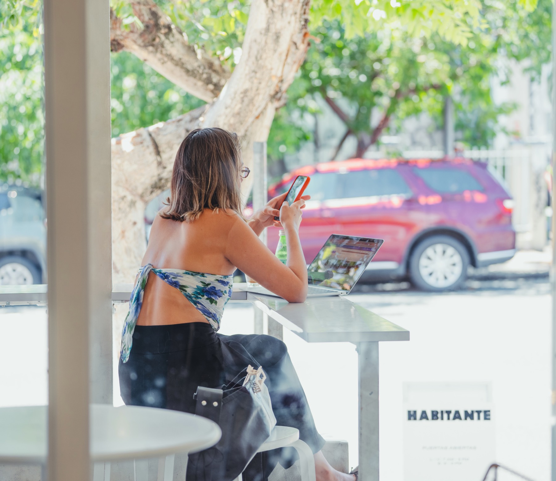 Clienta con laptop en la barra de la ventana, con el árbol y la calle afuera