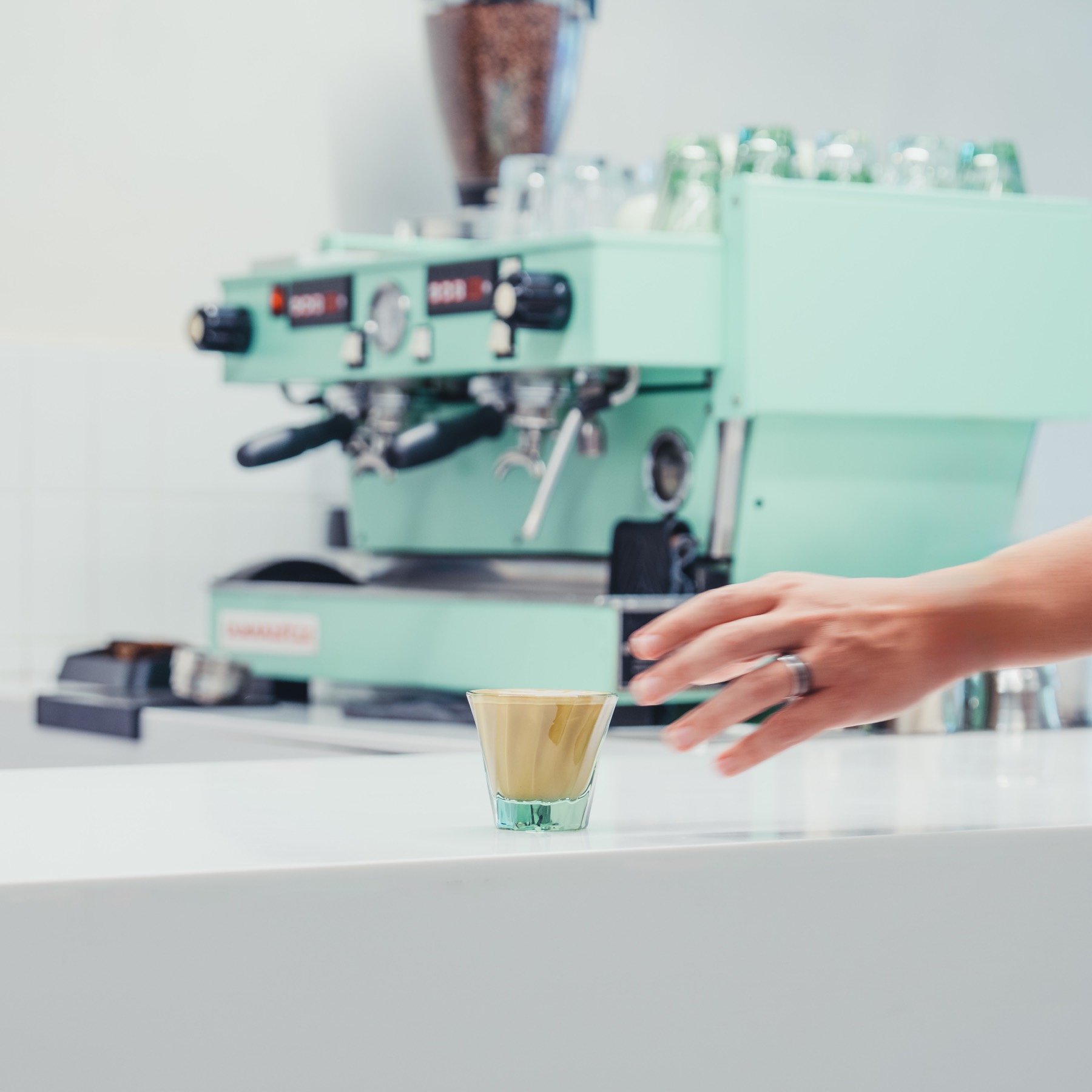 Cortado en vaso pequeño frente a la máquina de espresso color menta